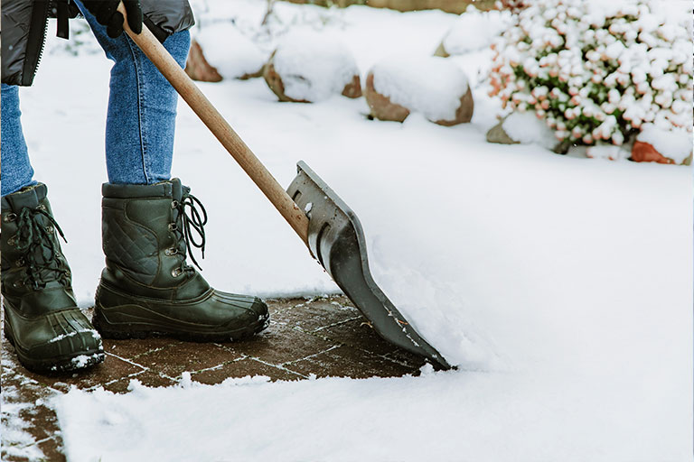 Image of a woman clearing snow from pathway with a snow shovel.
