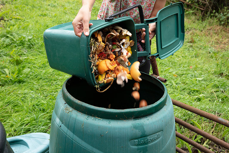 A lady putting her pre-collected kitchen scraps into a compost bin. 